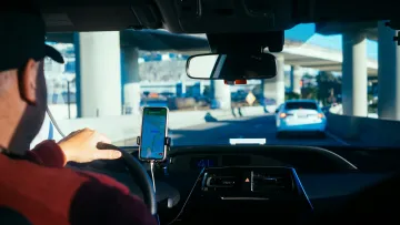 Driver using smartphone GPS navigation while driving on a city highway underpass during daytime.