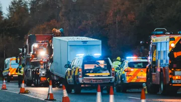 Emergency vehicles with flashing lights and safety cones at a roadside incident during twilight hours.