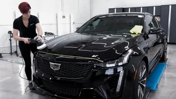 Person polishing a shiny black Cadillac car inside a clean garage or detailing shop.
