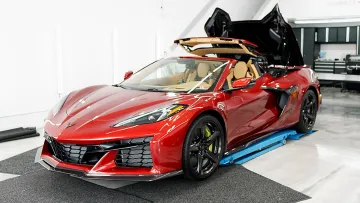 Red convertible sports car with black wheels and tan interior in a bright garage with roof partially open