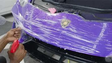 Person applying protective film on purple Lamborghini front bumper for paint protection.