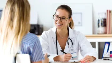 Smiling female doctor with glasses consulting a female patient in a bright medical office.