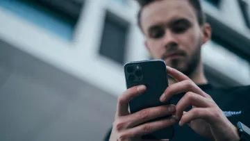 Young man using a smartphone outdoors in an urban setting with modern buildings in the background