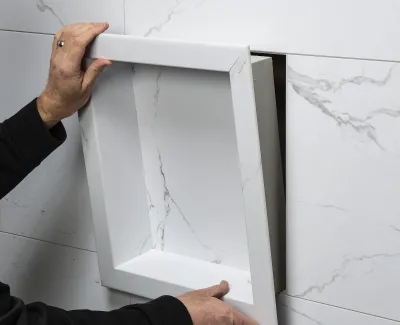 Hands installing a marble-patterned access panel matching the wall tiles for seamless concealment.