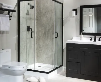 Modern bathroom with glass shower enclosure, black vanity, mirror, toilet, and slippers on tile floor