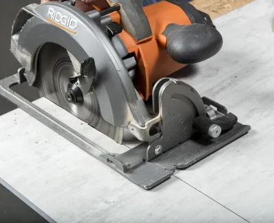 Close-up of a Ridgid circular saw cutting a white tile with a person's hand guiding the tool