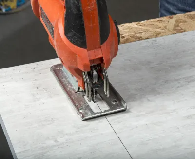 Close-up of an orange jigsaw cutting a straight line on a white wooden board in a workshop.