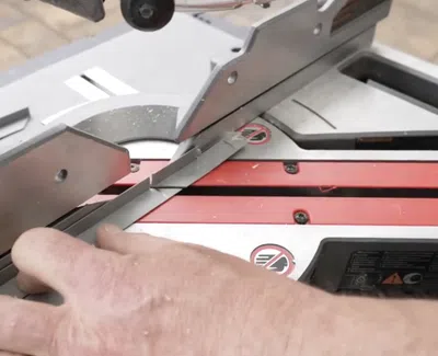 Close-up of hand operating a precision miter saw cutting a piece of wood at an angle.
