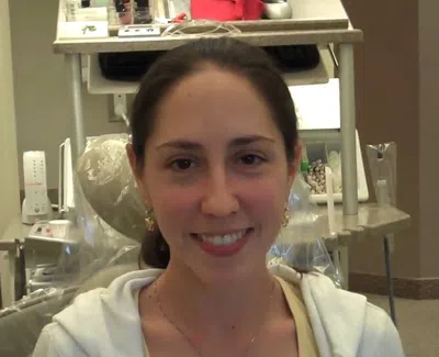 Smiling woman with dark hair sitting in a dental office chair in a dental clinic environment.