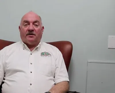 Middle-aged man in white shirt sitting in a brown leather chair against a plain wall in an indoor setting