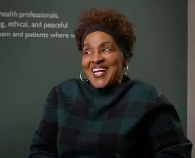 Smiling woman in checkered sweater sitting in a room with inspiring dental care text and flower vase.
