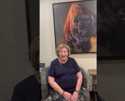 Smiling woman seated in armchair under large painting of a bison with warm tones on wall.
