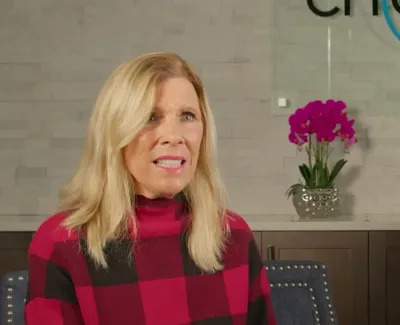 Woman in red and black checkered sweater seated in front of a dental office sign and orchid plant.