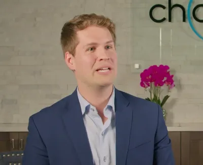 Young man in blue suit speaking in modern dental office with purple orchids and Chasoler Dentistry logo.