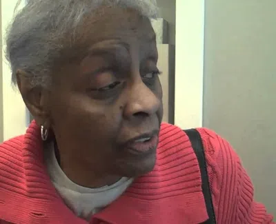 Elderly woman with short gray hair wearing a red sweater and looking to the side in an indoor setting