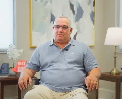 Middle-aged man wearing glasses and blue polo sitting in a modern living room with awards and lamp.