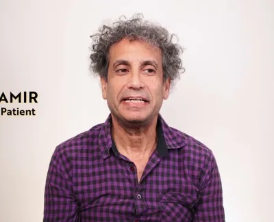 Middle-aged man with curly gray hair wearing a purple checkered shirt against a plain background.