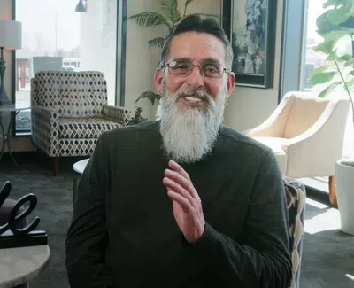 Smiling elderly man with gray beard sitting in a cozy room with modern chairs and a table sign saying Smile