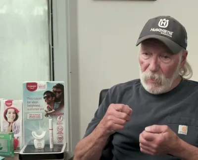 Older man wearing a Husqvarna cap sitting and talking in a dental office with promotional displays in background