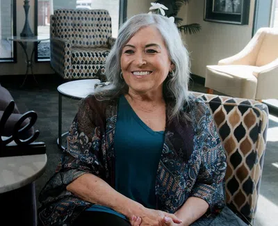Smiling senior woman sitting in a cozy living room with stylish chairs and a decorative Smile sign.