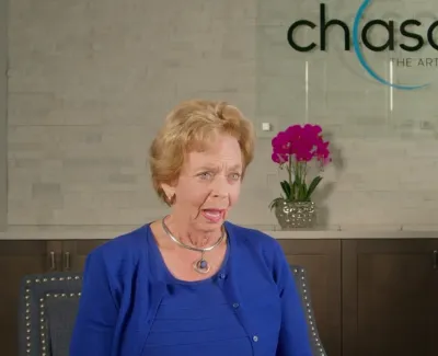 Older woman speaking in a dental office with Chasolen logo and vibrant pink orchids in the background