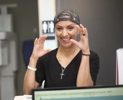 Smiling woman showing hand gestures sitting at a desk with computer and medical equipment in background