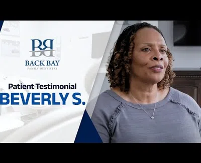 Back Bay Family Dentistry patient Beverly S. shares her testimonial in a clinical setting with dental branding.