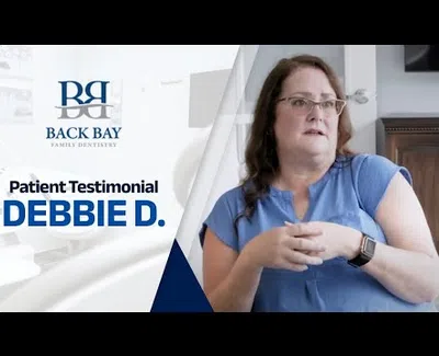 Patient testimonial from Debbie D. at Back Bay Family Dentistry with woman in blue shirt speaking.