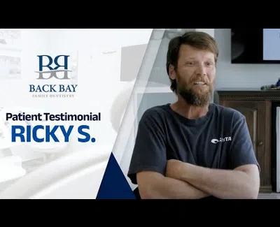 Smiling man with beard shares a patient testimonial for Back Bay Family Dentistry in a bright office setting