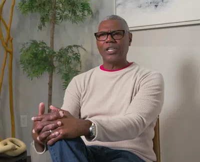 Middle-aged man in glasses sitting in a modern room with plants and decorative wooden sticks