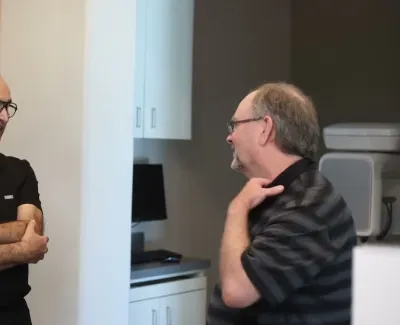 Doctor in black scrubs talking and smiling with a middle-aged male patient in a medical office.