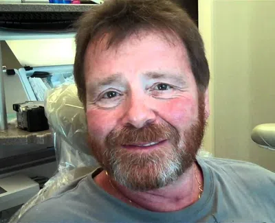 Smiling middle-aged man with beard sitting in a dental office chair with dental equipment in the background