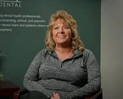 Smiling woman sitting in dental office with text about dental care and plants in the background