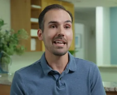Man in blue polo shirt speaking inside a modern dental office with plants and flowers in the background