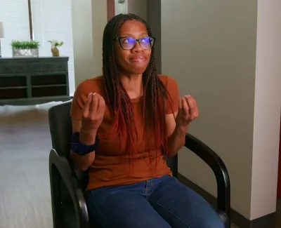 Young woman with glasses sitting in a chair gesturing with hands in a modern office setting