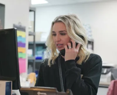 Blonde woman talking on phone while working at computer desk in organized office space.