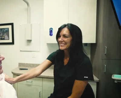 Smiling healthcare worker comforting elderly man in a medical office with framed pictures on the wall.