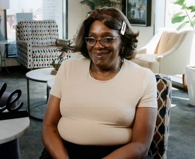 Smiling woman wearing glasses and a hair clip seated in a modern living room with a smile sign on the table.