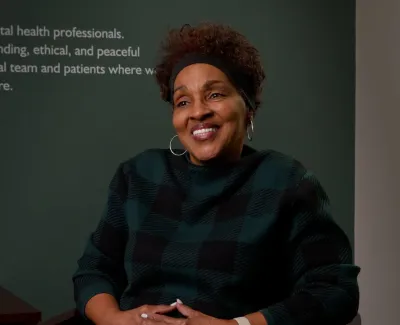Smiling woman in a checkered sweater sitting in an office with flowers and a plaque on the table.