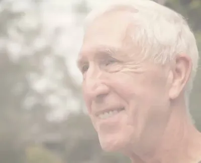 Smiling elderly man with white hair outdoors, blurred natural background, looking to the side