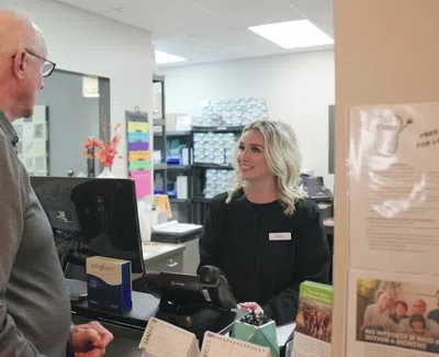 Elderly man consulting with a smiling female receptionist at a modern office reception desk.