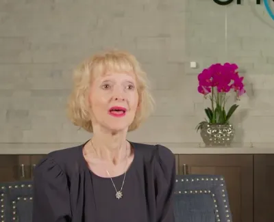 Mature woman speaking in a modern, elegant dental office with orchid and branded wall background