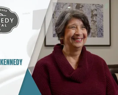 Smiling woman shares her positive testimonial about Kennedy Dental in a bright, professional setting.