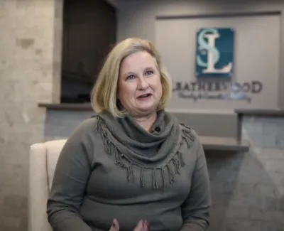 Smiling woman in gray sweater sitting in modern office with Lathropwood logo on the wall behind her.