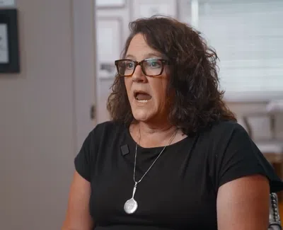 Woman with glasses and curly hair speaking in an indoor setting with framed picture in background