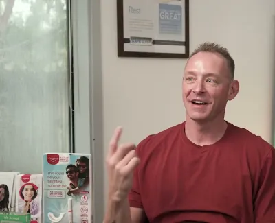 Smiling man in red shirt sitting in dental office with service list and product displays in background