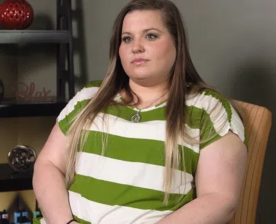 Young woman in green and white striped shirt sitting in chair with shelf and decorative items behind her