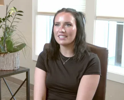 Young woman with dark hair sitting in an office chair near a window and a table with houseplants.