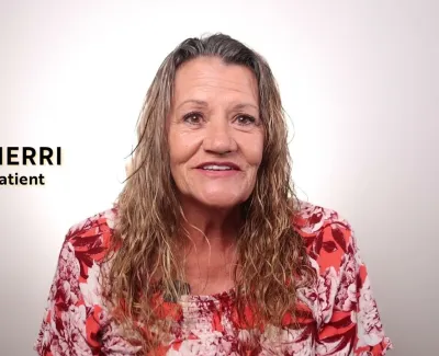 Smiling woman named Sherri identified as patient wearing a red and white floral top on a white background.