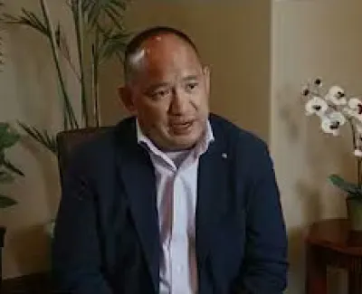 Man in business attire seated indoors with plants and a small table with orchid and brochure in background